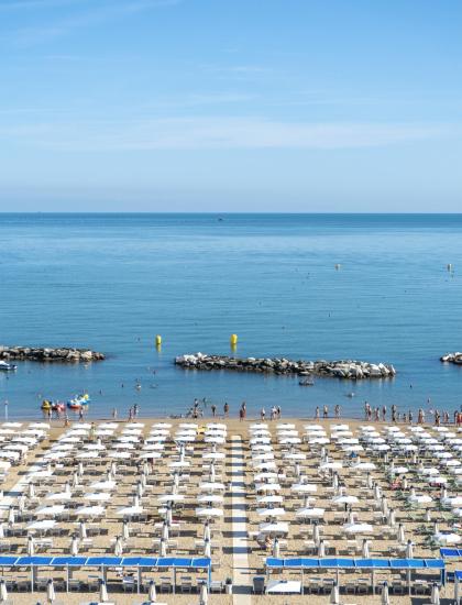 Spiaggia affollata, ombrelloni bianchi, mare calmo, cielo azzurro, giornata estiva perfetta.