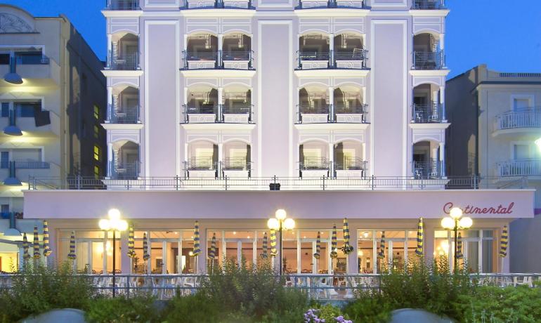 Hotel elegante con balconi, illuminato di notte, circondato da un giardino fiorito.