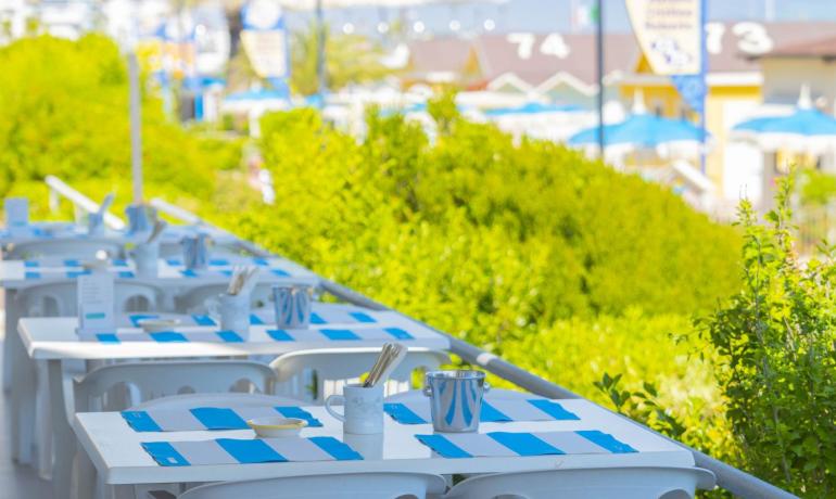 Tavoli all'aperto con tovagliette blu e bianche, vista sul mare.