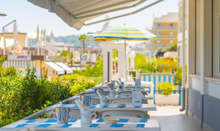 Terrazza con tavoli apparecchiati e ombrellone, atmosfera estiva e rilassante.
