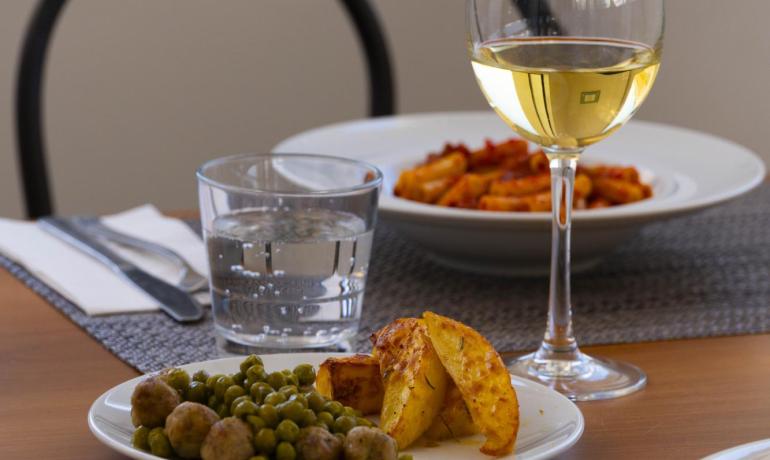 Tavola apparecchiata con vino, patate arrosto, piselli e pasta, atmosfera accogliente.