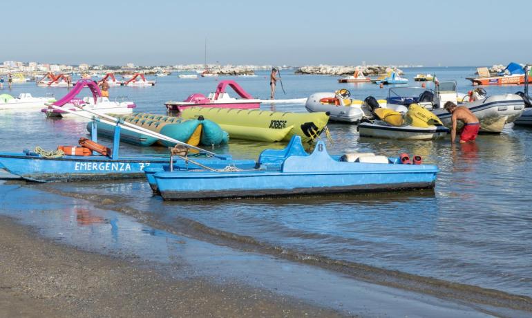 Spiaggia con pedalò e gonfiabili colorati sul mare calmo.