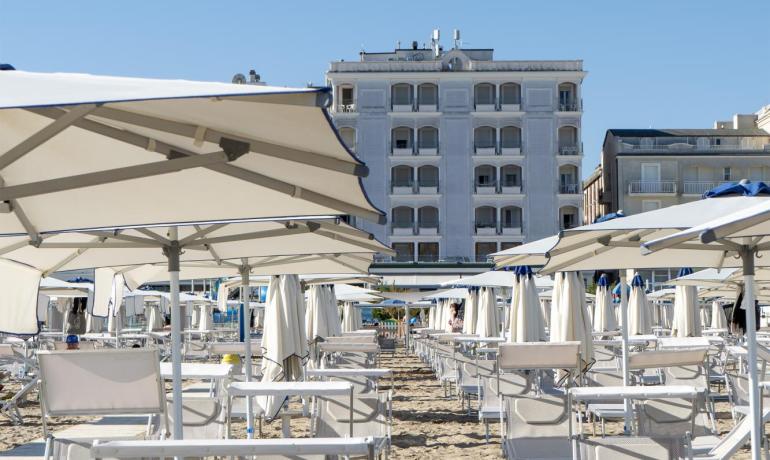 Spiaggia soleggiata, ombrelloni bianchi, cielo blu, atmosfera rilassante e vacanziera.