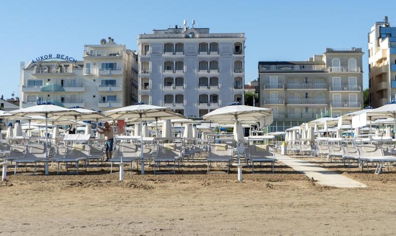 Spiaggia deserta, ombrelloni chiusi, cielo limpido e palazzi sullo sfondo.