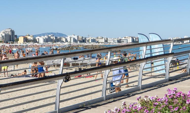 Spiaggia affollata con fiori e città sullo sfondo.