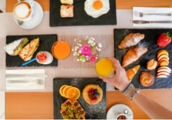 Colazione elegante con croissant, frutta, spremuta e caffè su piatti neri.