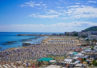 Spiaggia affollata sotto un cielo azzurro, ombrelloni colorati e mare calmo, estate vibrante.