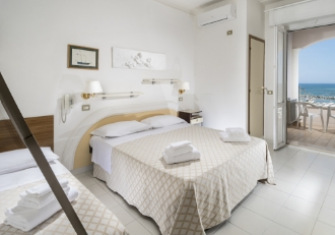 Camera d'albergo luminosa con vista mare, letti matrimoniali e balcone.