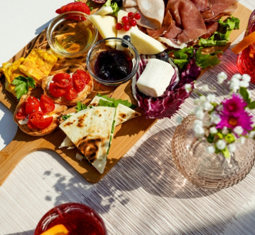 Tagliere con salumi, formaggi, frutta, pane e salse, decorato con fiori.