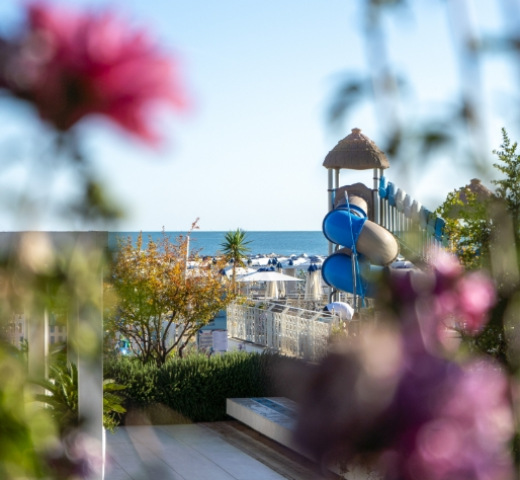 Vista sulla spiaggia con scivolo blu e fiori in primo piano.