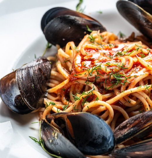 Piatto di pasta al ragù con bicchiere di vino bianco su tavola apparecchiata.