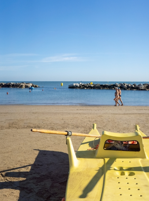 Spiaggia serena, mare calmo, cielo limpido, pedalò giallo, coppia passeggia, atmosfera rilassante.