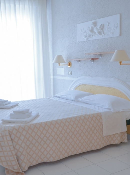 Camera luminosa con letto matrimoniale, lenzuola bianche e decorazione murale.