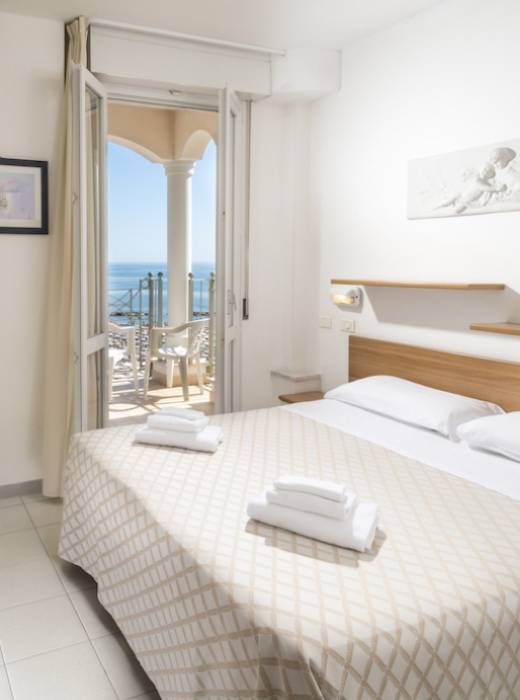 Camera luminosa con vista mare, letto matrimoniale e balcone privato.