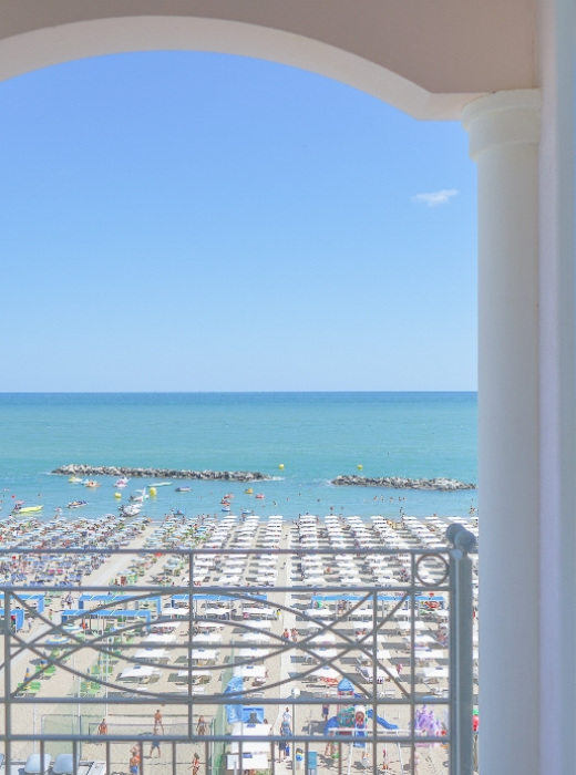 Vista su spiaggia affollata con ombrelloni, mare e cielo azzurro.