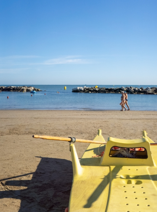 Spiaggia sabbiosa con pattino giallo e due persone che camminano sul bagnasciuga.
