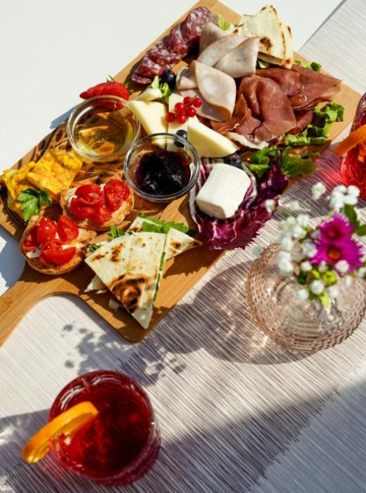Tagliere colorato con salumi, formaggi, bruschette e cocktail. Atmosfera estiva e conviviale.