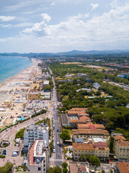 Spiaggia affollata, mare azzurro, città vivace, natura verde, cielo sereno, estate vibrante.