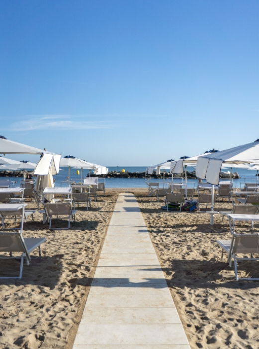 Spiaggia soleggiata con ombrelloni bianchi, mare calmo e cielo limpido, atmosfera rilassante.