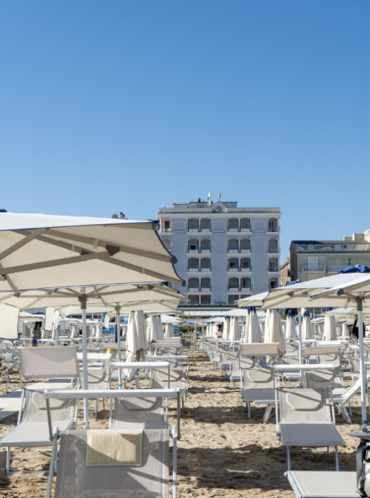 Spiaggia soleggiata, ombrelloni bianchi, lettini vuoti, cielo azzurro, atmosfera estiva e rilassante.