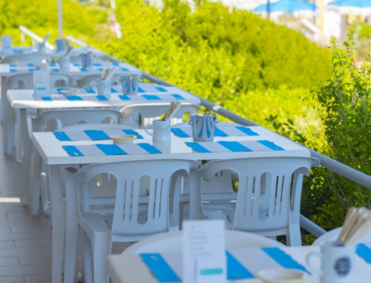 Tavoli bianchi all'aperto con tovagliette blu, immersi nel verde.