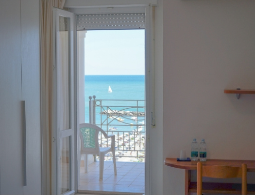 Vista sul mare da una stanza con balcone e sedia bianca.