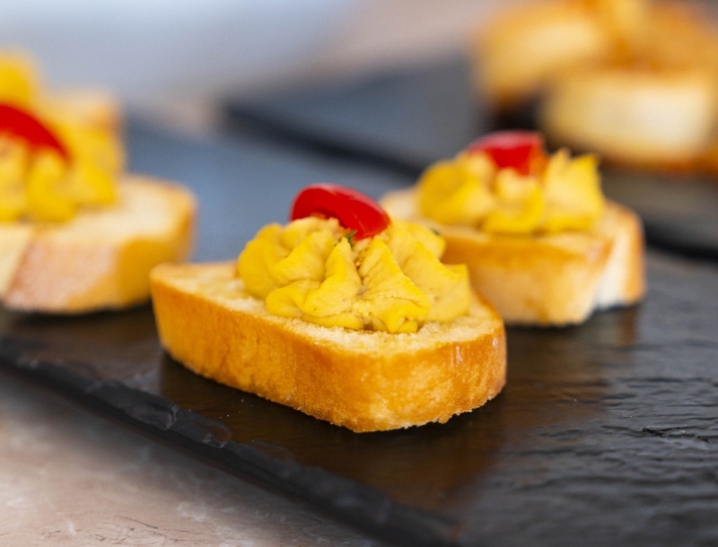 Crostini con crema di zucca e peperone rosso su piatto di ardesia.