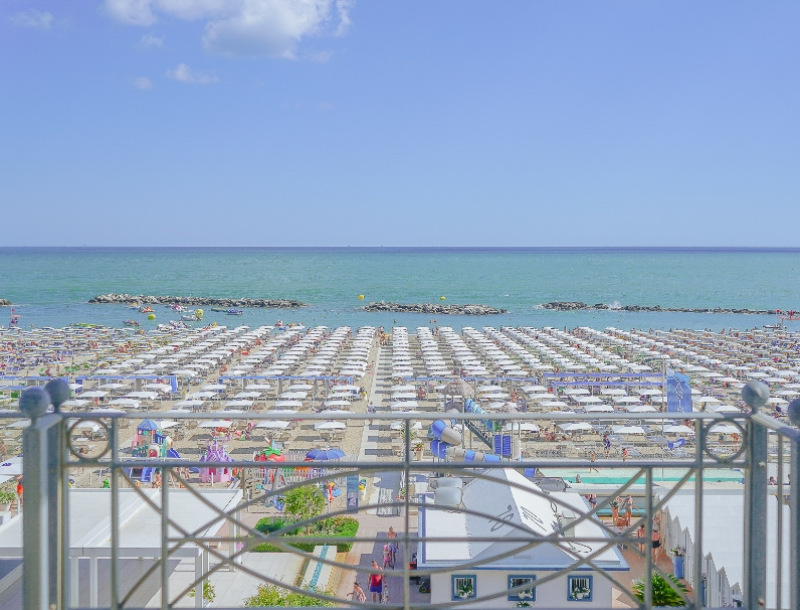 Spiaggia affollata con ombrelloni bianchi, mare calmo e cielo sereno.
