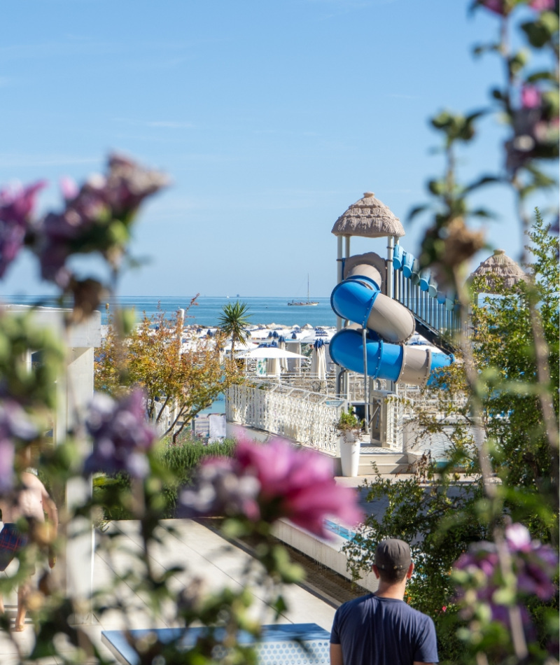 Scivolo blu, mare azzurro, fiori colorati; atmosfera estiva e gioiosa sulla spiaggia.