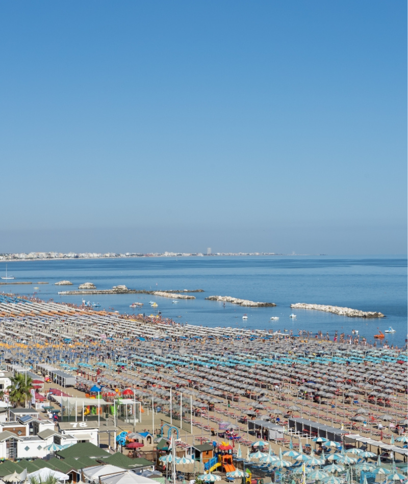 Spiaggia affollata di ombrelloni colorati, mare calmo e cielo azzurro limpido.