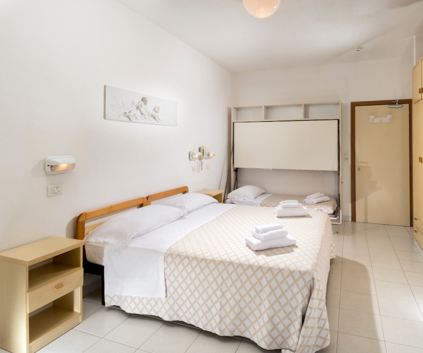 Camera d'albergo con letto matrimoniale, letto singolo e arredi semplici.
