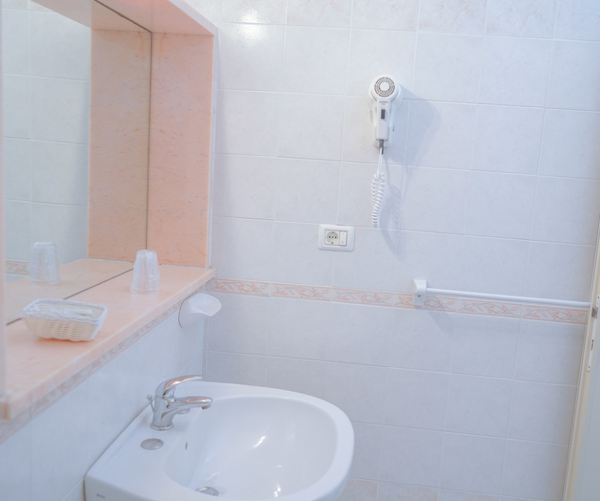 Bagno con specchio, asciugacapelli, lavandino e accessori su piastrelle chiare.