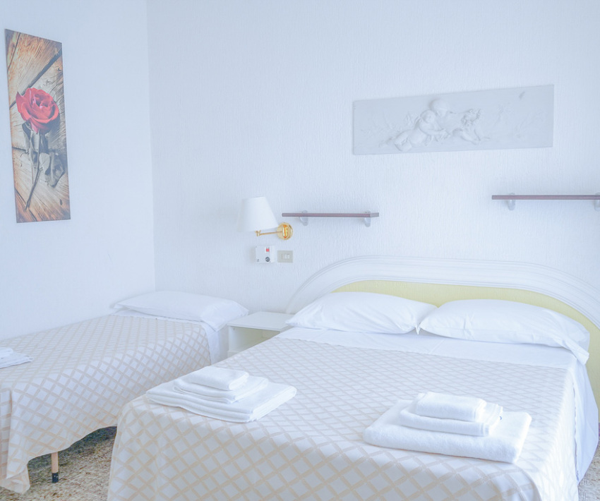 Camera luminosa con due letti, decorazioni semplici e asciugamani piegati sul letto.