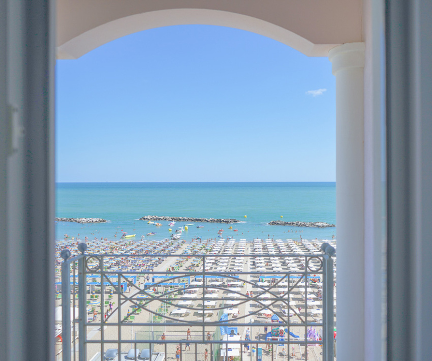 Vista su una spiaggia affollata e mare calmo da un balcone.