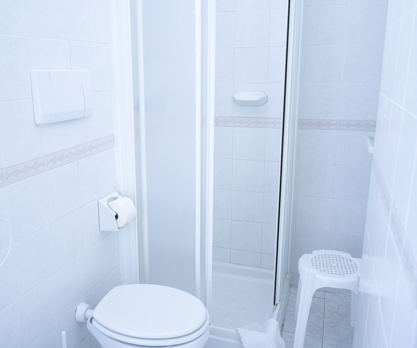 Bagno bianco con doccia, wc, carta igienica e sgabello.