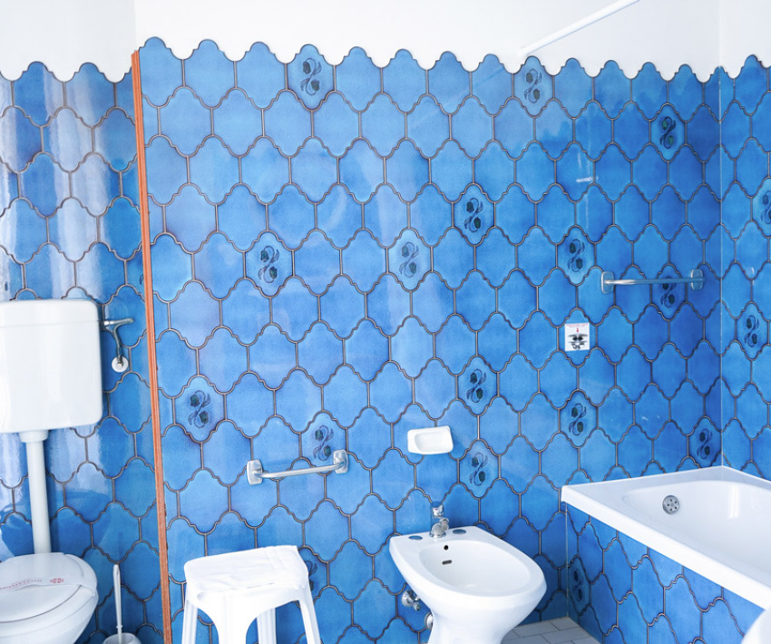Bagno vintage con piastrelle blu, vasca, bidet e WC con cassetta alta.