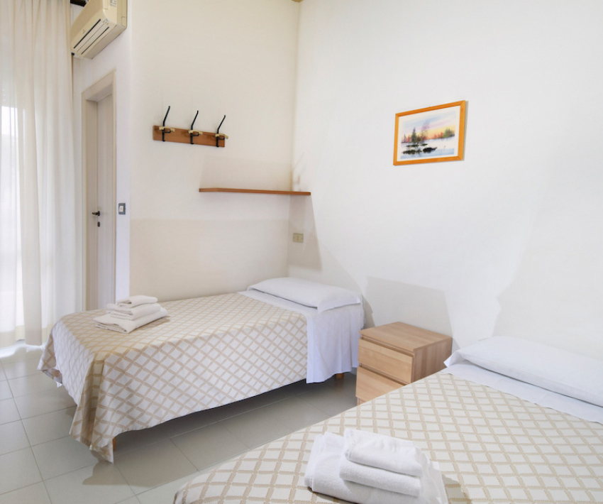 Camera luminosa con letto matrimoniale, armadio aperto, scrivania e televisore.