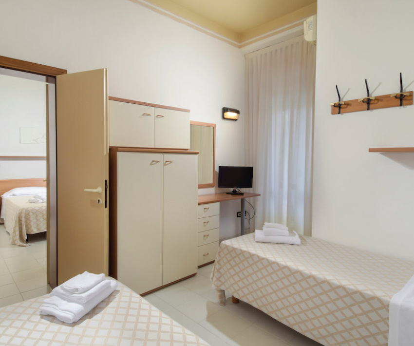 Camera doppia con letti singoli, armadio, TV e bagno annesso.