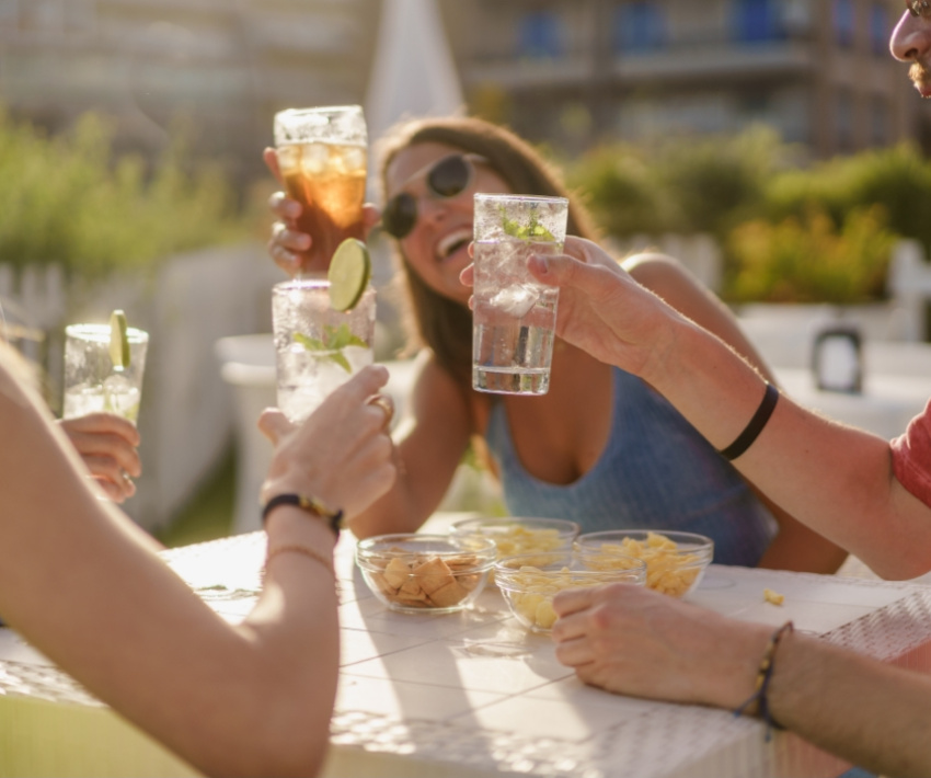 Amici sorridenti brindano all'aperto, bicchieri alzati, atmosfera di gioia e convivialità estiva.